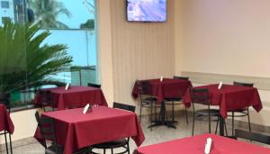 ein Zimmer mit roten Tischen und Stühlen und einem Fernseher in der Unterkunft Domus Hotel Cidade Nobre - Ipatinga in Ipatinga
