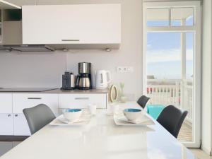 a white kitchen with a long white table and chairs at Ferienwohnung Baltic Lounge 53 in Haffkrug +7 photos