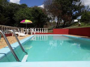 a swimming pool with an umbrella and a table and chairs at Chale da Pousada Curió in Ibiúna