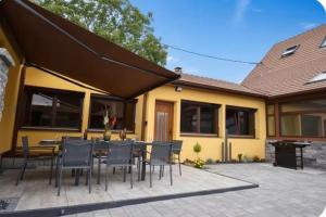 a patio with a table and chairs and a yellow house at Le Courlis du Ried in Grussenheim