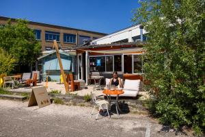 Eine Frau sitzt an einem Tisch vor einem Gebäude in der Unterkunft DE BUITENKANS urban camping - unique cabins in Rotterdam