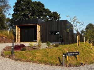 a small black building on a hill with a sign at Cadderlie Cabin - Luxury Woodland Escape with Hot Tub Near Oban in Oban
