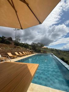a large swimming pool with chairs and an umbrella at Hotel Cariguá in Barichara