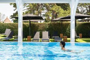 a person swimming in a swimming pool with umbrellas at Renaissance Paris Hippodrome de St. Cloud Hotel in Rueil-Malmaison