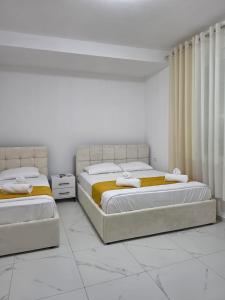 two beds in a bedroom with white walls and white floors at Aer Rooms Peshkopi in Peshkopi