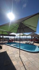 a swimming pool with a green umbrella and chairs at Pousada beira mar e sol in Tibau
