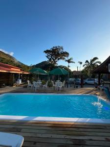 a swimming pool with tables and chairs and umbrellas at Hospedagem Ratzke in Paraty