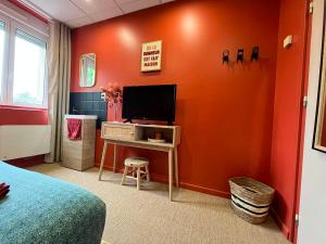 a bedroom with an orange wall with a television on a table at Le pré des noisettes in Angomont