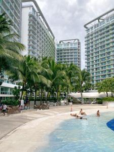 two people in a pool with palm trees and buildings at Azure Urban Resort Residences St Tropez Tower Near SM Bicutan with Wave Pool in Manila