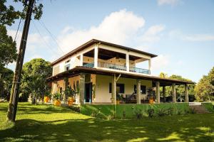 a white house with a porch on a grass field at Hotel Pousada Flor de Alecrim - Goiana in Goiana