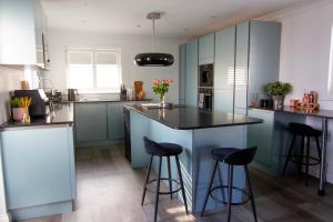 a kitchen with blue cabinets and black counter stools at Coopers by the Coast in Selsey +19 photos