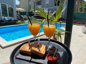 two glasses of orange juice and toast on a tray next to a pool at Vila DeLux in Negotin