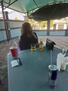 a woman sitting at a table with a drink at The John's Park in Mwanza