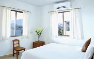 a white bedroom with windows and a bed and a chair at Savana Lake Resort in Nashik