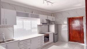 a white kitchen with white cabinets and a refrigerator at SAOB Property- South A in Germiston +13 photos