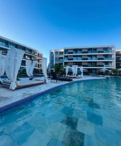a swimming pool with chairs and a building at Resort de Luxo em Muro Alto - Porto de Galinhas in Ipojuca
