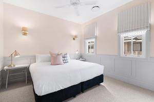 a white bedroom with a bed and a desk and windows at Farmhouse Hunter Valley in Pokolbin +17 photos