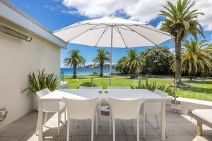 a patio with a white table and chairs and an umbrella at Beachfront 25 The Strand Moana in Waiheke Island