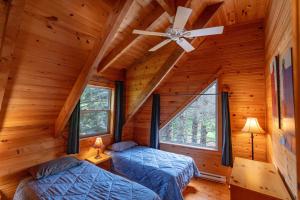 two beds in a log cabin with a ceiling fan at Avonlea Forest Hill Cottages in New Glasgow