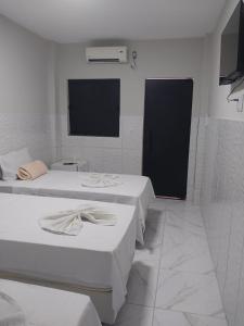a white room with three beds and a black door at Pousada Triângulo in Juazeiro do Norte