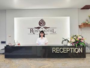 a woman standing behind a counter in front of a sign at Rosy Hotel Dương Nội in Hà Ðông