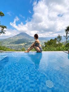 Eine Frau sitzt am Rand eines Schwimmbeckens in der Unterkunft Pinggan Infinity - Private Pool Villa in Kintamani in Gretek