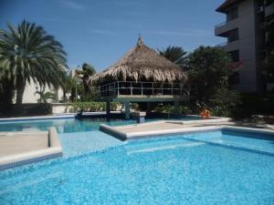 a swimming pool with a thatch umbrella and a resort at Exclusiva suite en Hotel Marbellamar in Pampatar