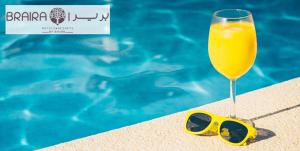 a glass of orange juice and sunglasses next to a swimming pool at Braira Al Nakheel in Riyadh