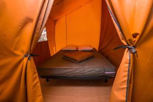 a bed in a tent with orange walls and curtains at Camping Onlycamp Les Peupliers in Lepin-le-Lac