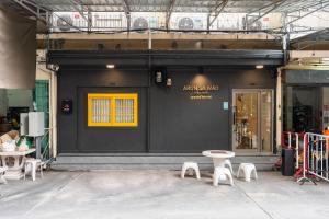 a store front with a yellow window and white stools at Arun Sa Wad - Chinatown House in Bangkok