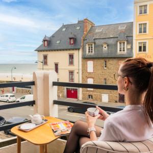 a woman sitting on a balcony with a cup of coffee at La Villa du Sillon by les Ambassadeurs - Saint Malo Plage in Saint Malo