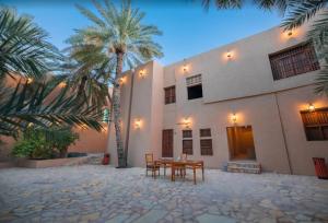 a table and chairs in front of a building with palm trees at Nomad Inn Al Bustan in Nizwa