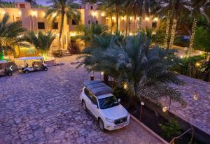 a white van parked in a courtyard with palm trees at Nomad Inn Al Bustan in Nizwa