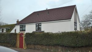a white house with a red door and a hedge at Bay Lodge in Birchington