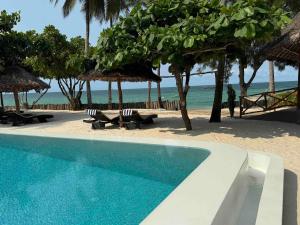 a swimming pool next to a beach with chairs and umbrellas at Amani Palms by Manolo Beach Resort in Uroa