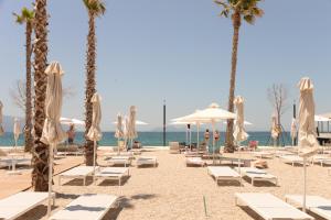 a beach with white chairs and umbrellas and palm trees at Esbjerg Hotel in Vlorë