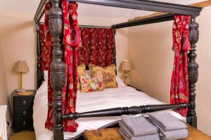 a bedroom with a four poster bed with red curtains at Finest Retreats - Lavender Cottage in Methwold