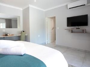 a white bedroom with a large bed and a flat screen tv at Meloding Guest House in Bela-Bela