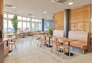 a restaurant with wooden tables and chairs and windows at B&B HOTEL Paris Roissy CDG Aéroport in Roissy-en-France