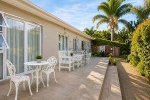 a patio with white tables and chairs and a palm tree at The Alchemist's Place in Oudtshoorn