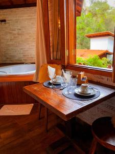 a wooden table with plates and glasses and a window at Chalés Montanha Serrana - Monte Verde in Monte Verde