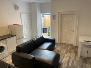 a living room with a black leather couch and a door at Elder Park Apartments in Glasgow