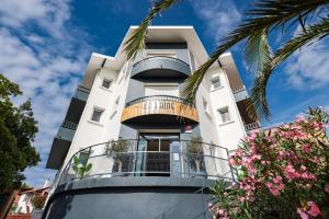 a white building with a balcony and palm trees at Hôtel La Baïne in Capbreton