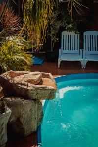 a swimming pool with two white chairs and a rock wall at Pousada Nanai in Foz do Iguaçu