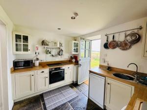 a kitchen with white cabinets and a sink at Charming cottage with loch and hill views nr Edinburgh in Cobbinshaw