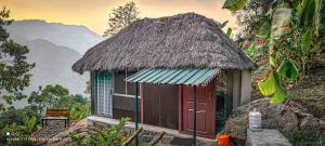 a small hut with a thatch roof with a window at The Cloud door in Perumālmalai