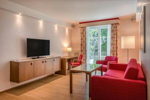 a living room with red chairs and a flat screen tv at Sheraton Grand Salzburg in Salzburg +156 photos