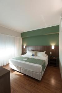 a bedroom with a large bed with a green wall at Firenze Business Hotel in Palhoça