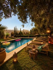 a pool with wooden benches and a group of tables at Dar Benyahya in Aït Zat