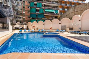 a large swimming pool with blue chairs and a building at Hanami Suite in Lloret de Mar